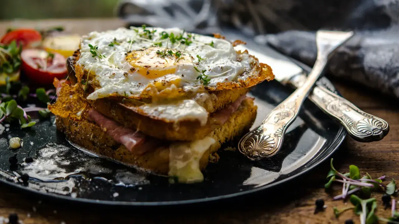Un croque-madame gourmand, un des plats typiques parisiens, avec un œuf au plat, jambon et fromage fondant, servi avec des tomates et des pousses.