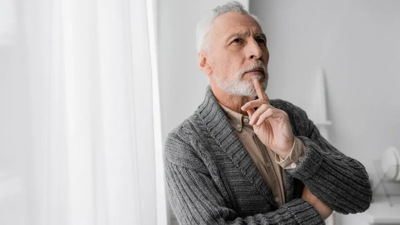 Uomo anziano con barba bianca, pensieroso, con un dito sul mento, forse valutando i risultati di un decadimento cognitivo test.