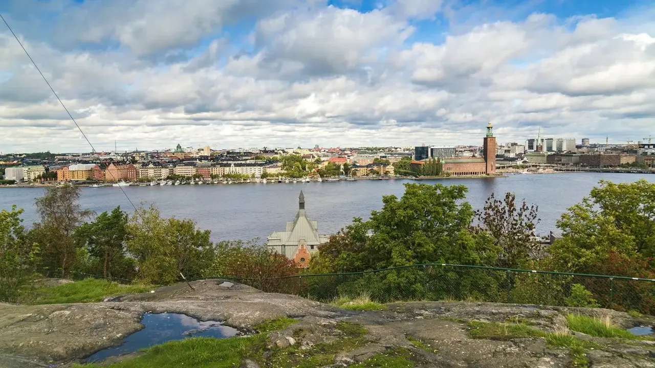 Vy över Riddarfjärden från Skinnarviksberget Stockholm, med Stadshuset i bakgrunden under en molnig himmel.