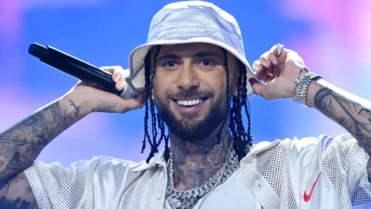 Malik Montana we Wrocławiu, w białym bucket hat, z mikrofonem w dłoni, uśmiecha się do fanów.
