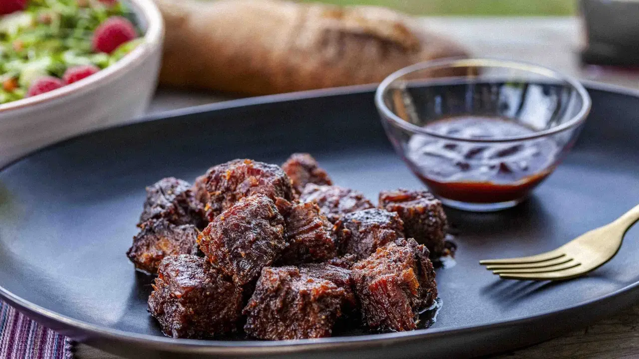 Saftige, karamellisierte **burnt ends** auf einem Teller mit BBQ-Sauce und Salat. Ein Fest für Fleischliebhaber!