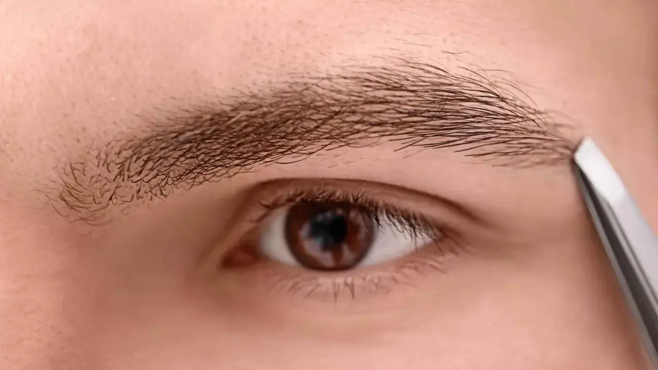 Un homme utilise une pince à épiler pour tailler un sourcil qui rebique, affinant son regard.