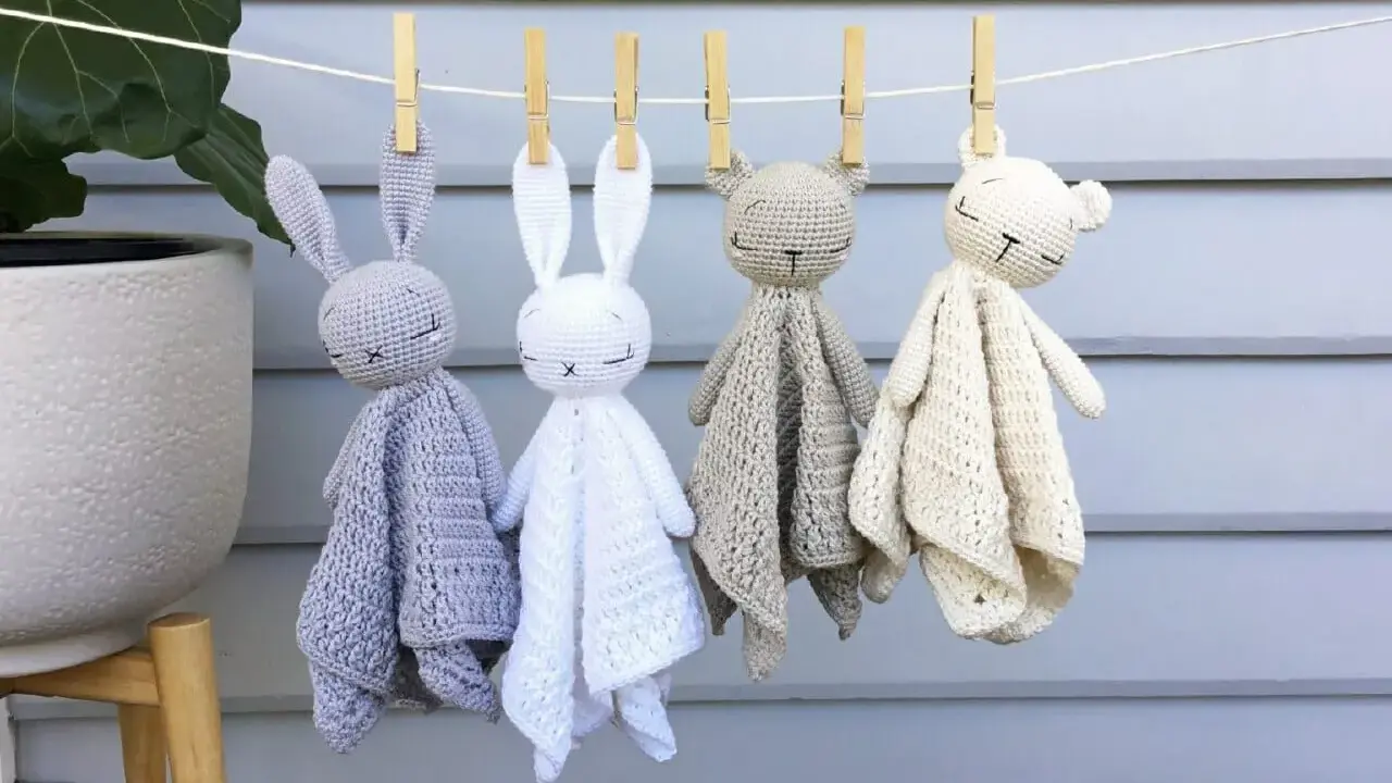 Cuatro adorables mantas de apego crochet, con forma de conejitos y ositos, cuelgan de una cuerda.