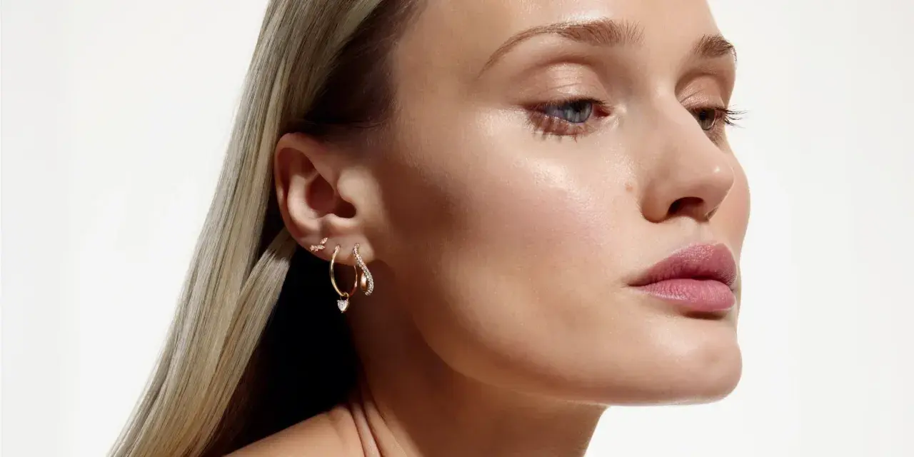 Delikatne kolczyki z kwiatami i serduszkiem, zdobiące ucho modelki, dodają subtelnego blasku.
