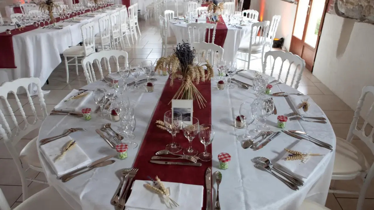 Une table dressée à la française, prête pour un événement. Nappes blanches, chemins de table bordeaux, vaisselle et couverts élégants, et une touche champêtre avec des épis de blé et de la lavande.