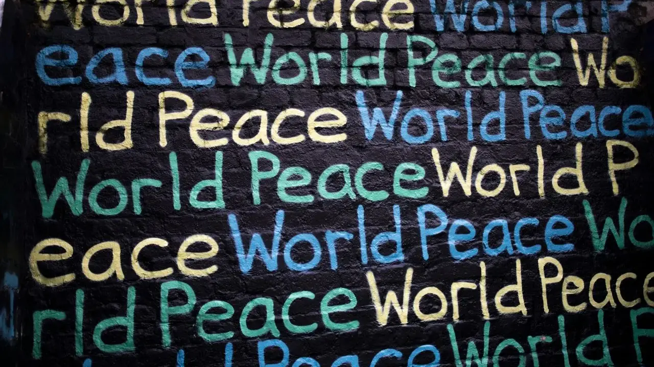 Un promemoria di Gianni Rodari: "Pace nel mondo" scritto in giallo, blu e verde su un muro di mattoni neri.