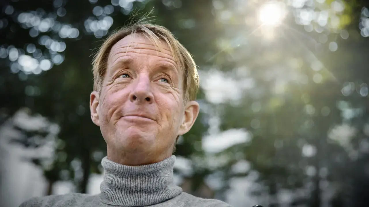 En leende man med rullstol, kanske en scen från filmer med Nils Hallberg, tittar upp mot solen.