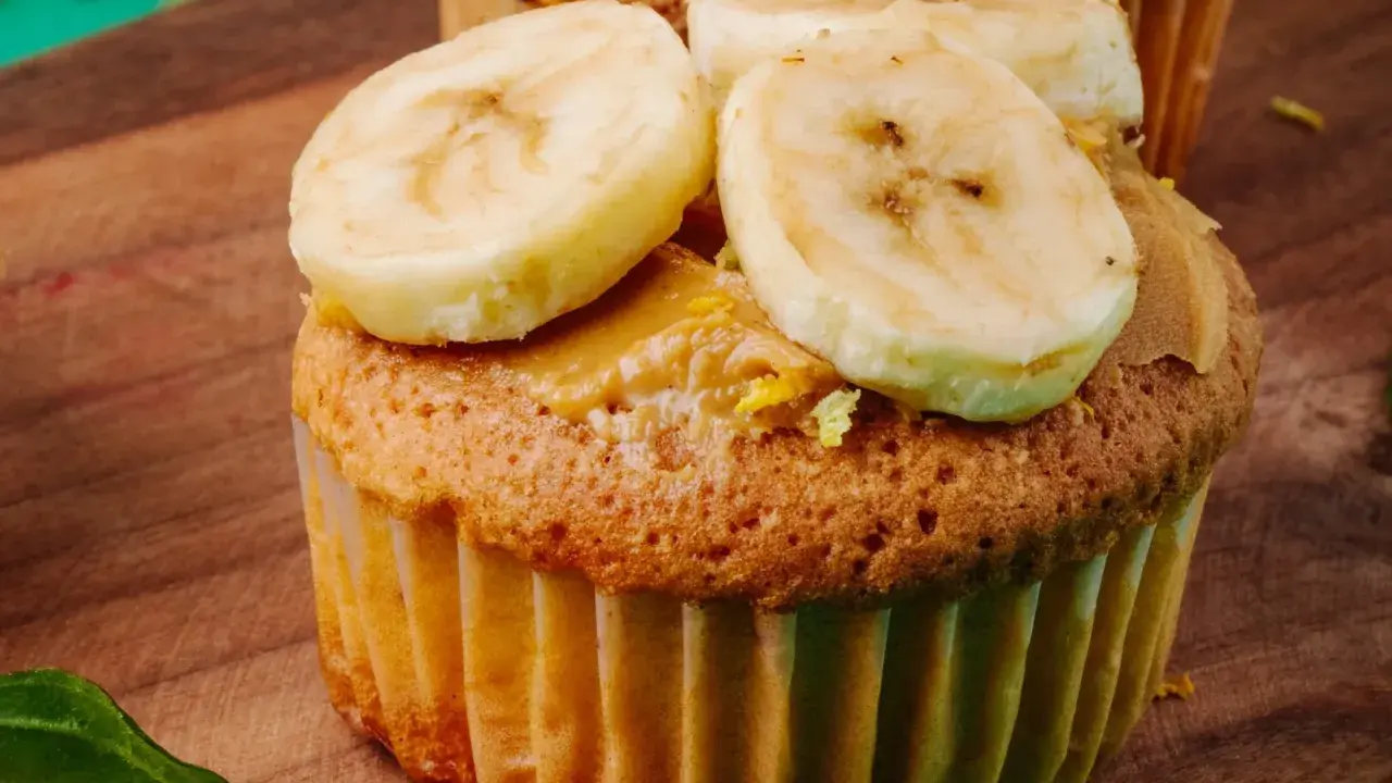 Pyszne muffinki bananowe fit z masłem orzechowym i plasterkami banana na drewnianej desce.