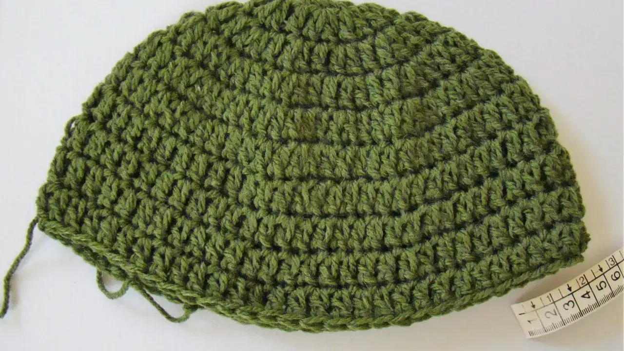 Gorro de lana verde tejido a mano, ideal para aprender como tejer un gorro de lana para principiantes. Cinta métrica al lado.