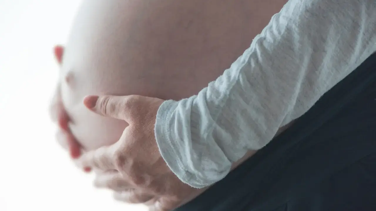 Dłonie obejmujące ciążowy brzuch, odczuwając ucisk na pęcherz w ciąży w II trymestrze.