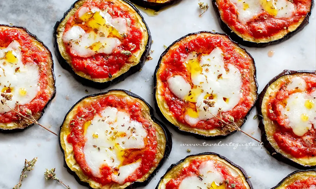 Pizzette di melanzane pronte per essere gustate, con pomodoro, mozzarella filante e un filo d'olio.