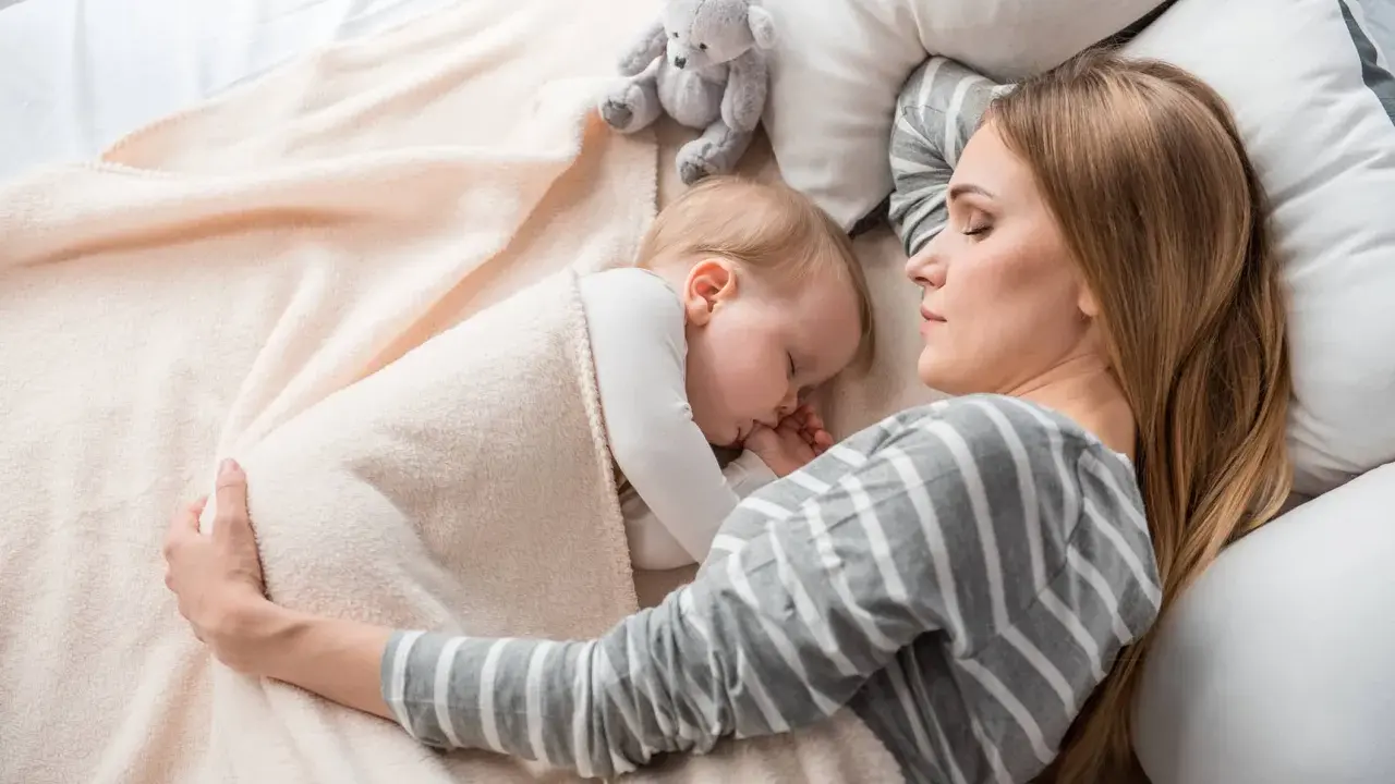 Mamma e bimbo dormono abbracciati, un tenero momento di co sleeping con un orsetto di peluche.
