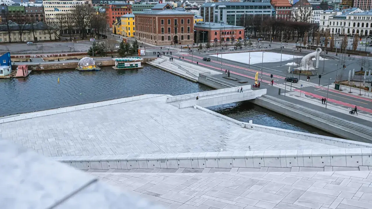 Widok z punktu widokowego Oslo na nowoczesną architekturę, wodę i plac z rzeźbą.