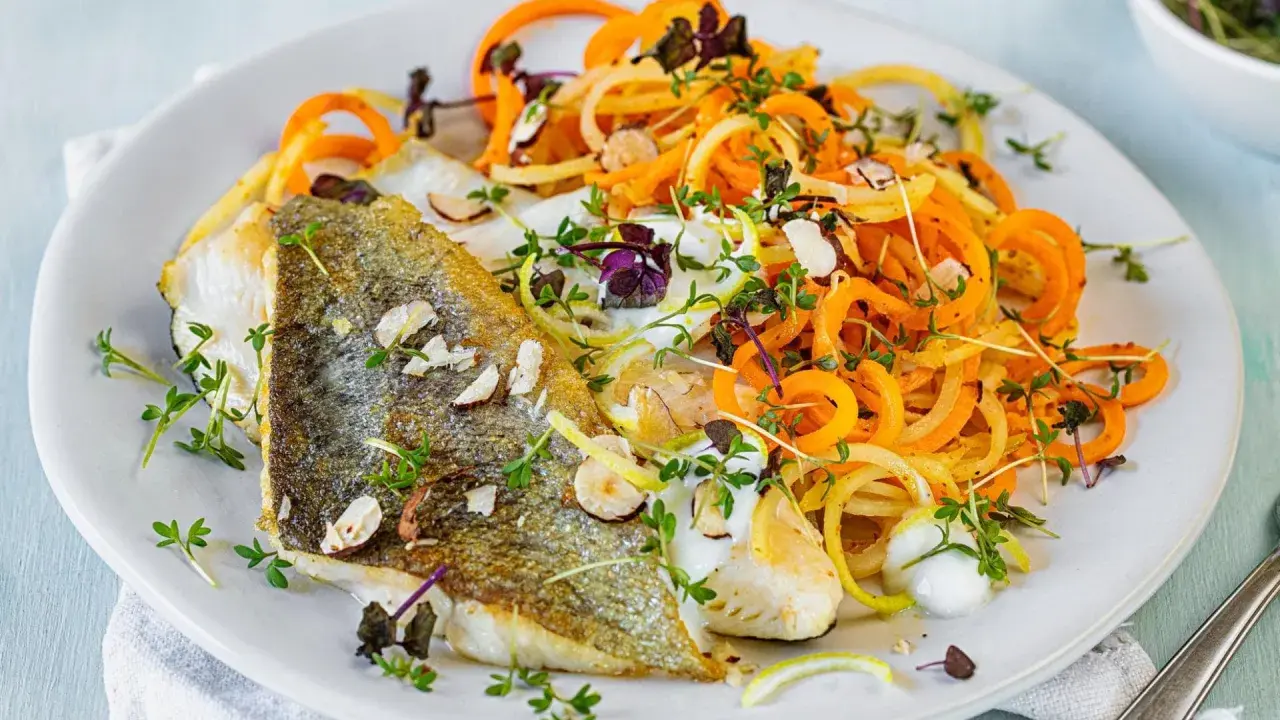 Gebratenes Fischfilet mit Spiralnudeln aus Karotten und Zucchini, garniert mit Kräutern und Mandelsplittern. Perfekt für leichte fasten rezepte.