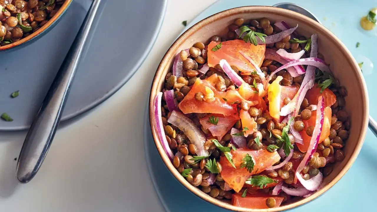 Salade de lentilles savoureuse avec des morceaux de saumon, des oignons rouges et du persil frais. Un plat coloré et nutritif.