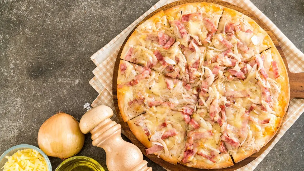 Flammekueche gourmande, garnie de lardons et d'oignons sur une base de fromage blanc crémeux. Un délice croustillant.