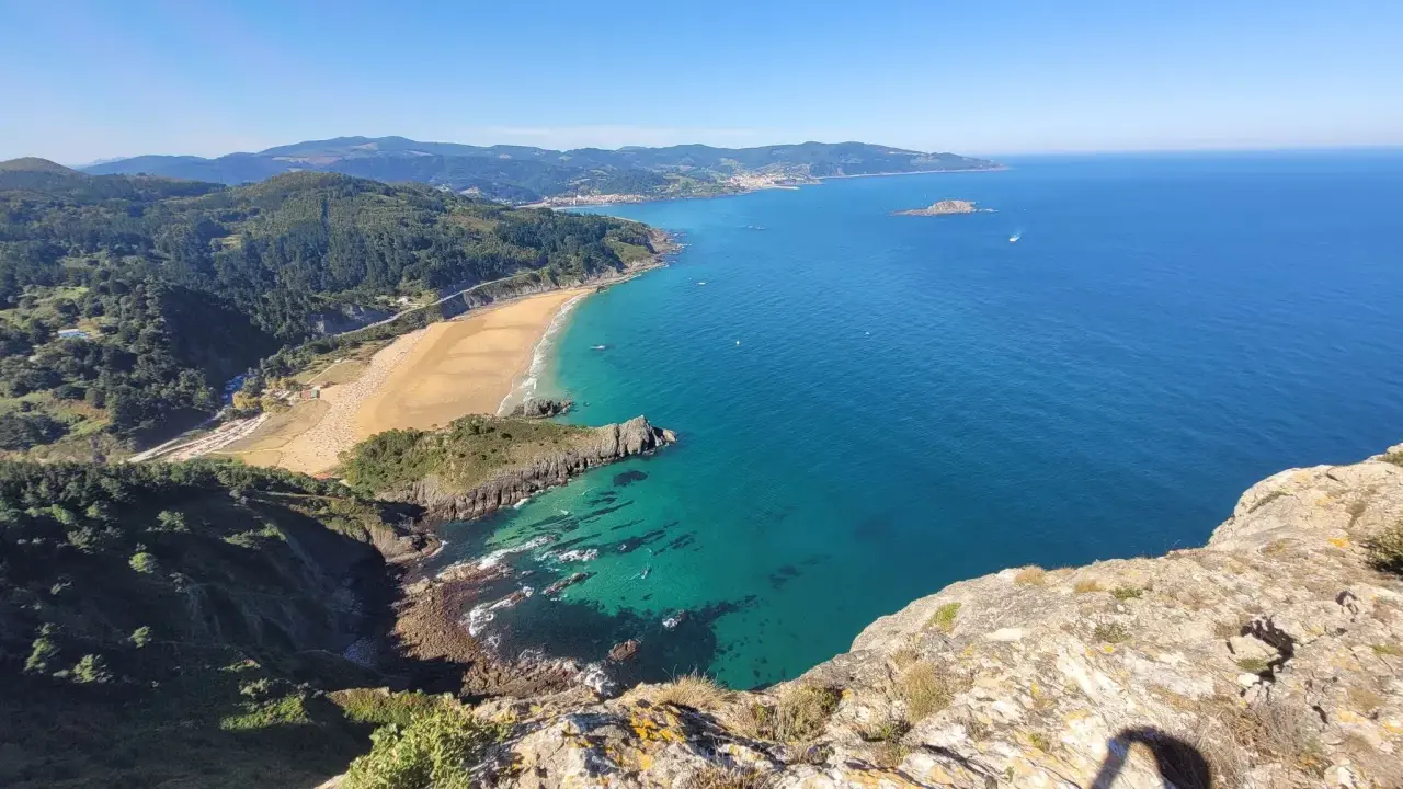Blick vom Berg auf eine Bucht mit Sandstrand und türkisfarbenem Meer. Perfekt für eine Wanderung im Baskenland.