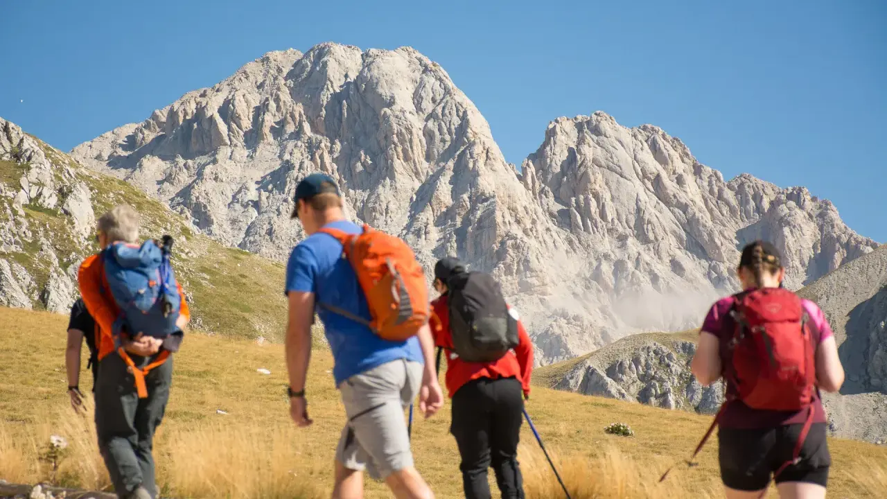 Escursionisti si dirigono verso un imponente corno grande, con zaini colorati e bastoncini da trekking.