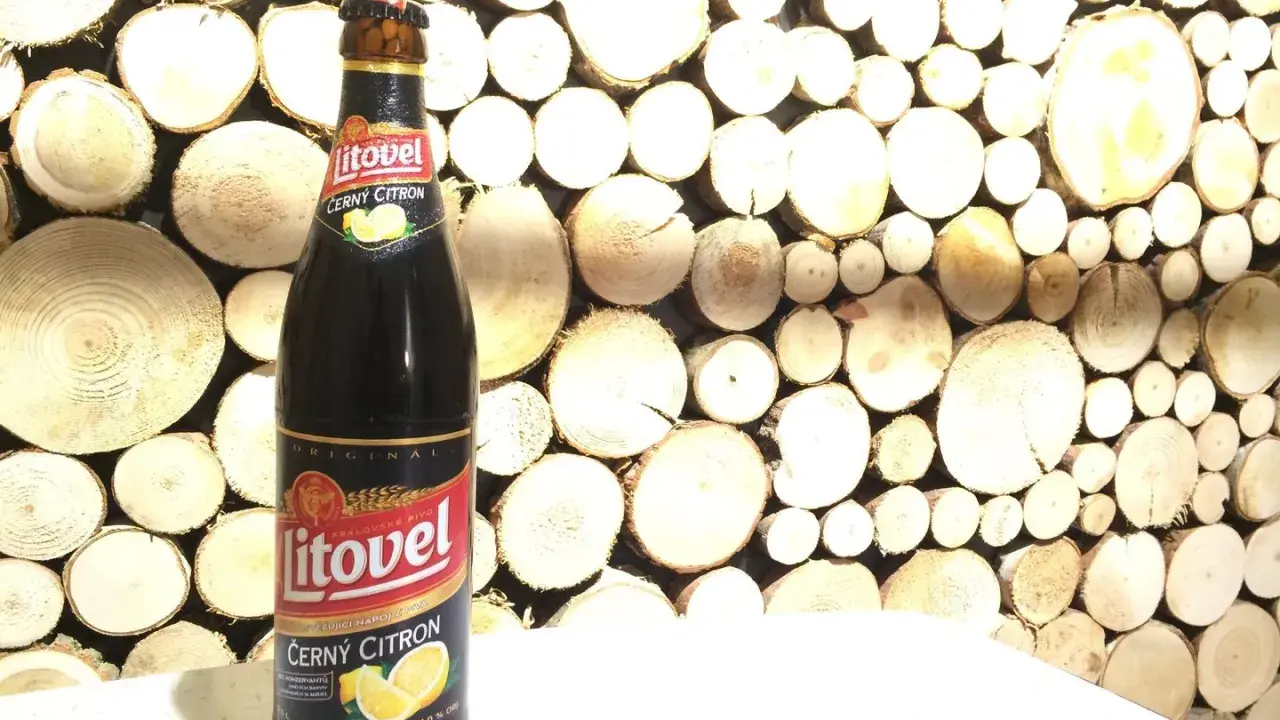 Butelka piwa Litovel Černý Citron na tle drewnianej ściany z plastrów drewna.