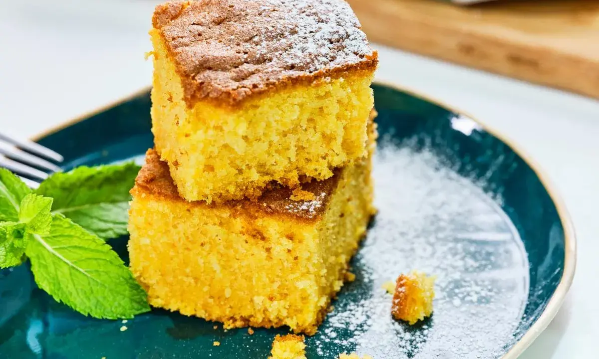Dos porciones de bizcocho de calabaza espolvoreadas con azúcar glas, acompañadas de hojas de menta fresca en un plato azul.