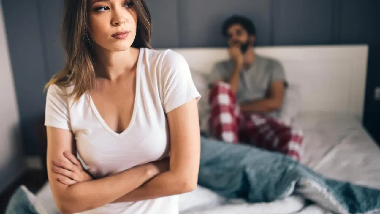 Kobieta zmartwiona, mężczyzna w tle. Problemy intymne, może uczulenie na spermę?