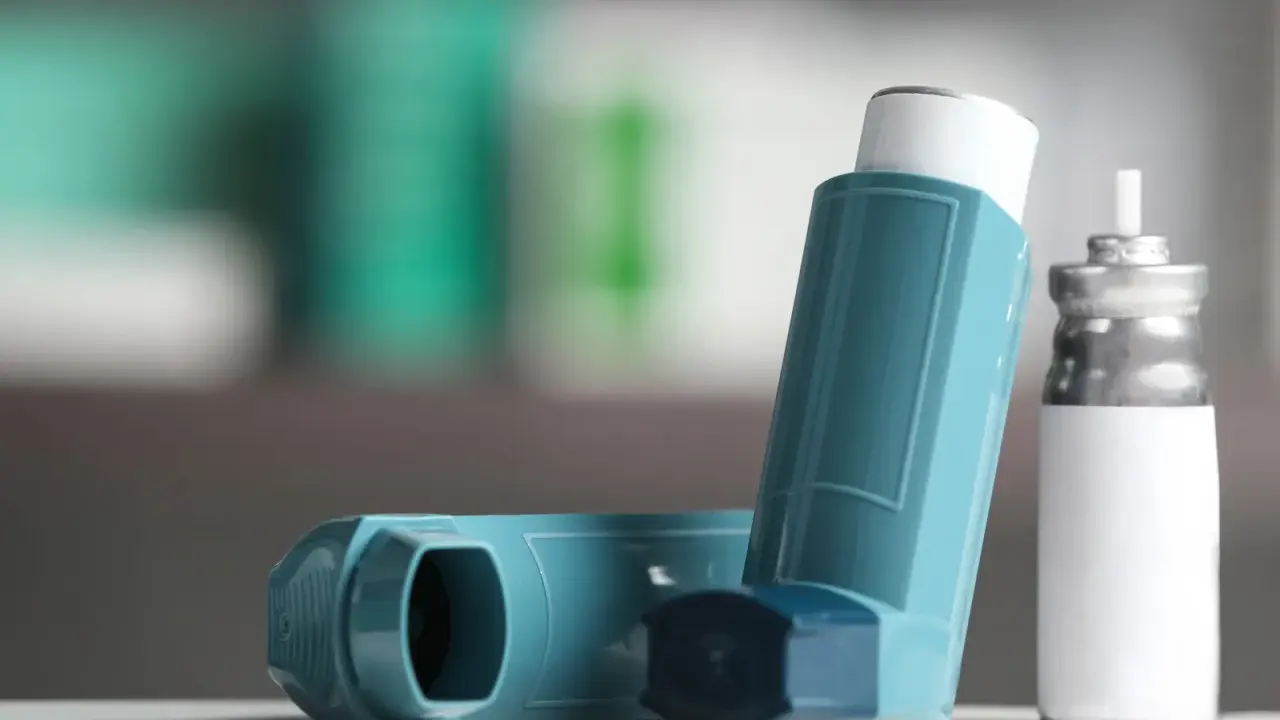 Zwei Inhalatoren, einer davon ein Symbicort-Spray, liegen auf einer weißen Oberfläche.