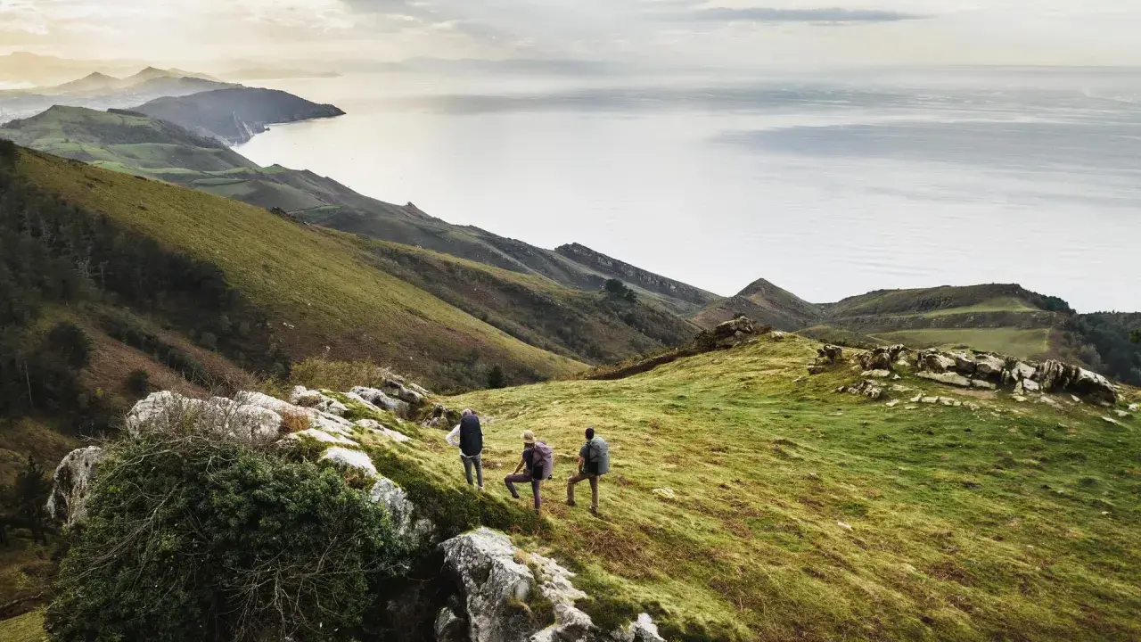 Trzech turystów podczas trekkingu na zielonym wzgórzu z widokiem na morze i góry.