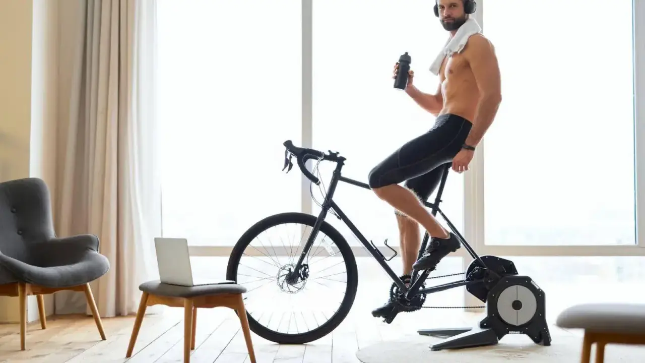 Mężczyzna w słuchawkach pije wodę, ćwicząc na rowerze stacjonarnym przy dobrej muzyce na rower.