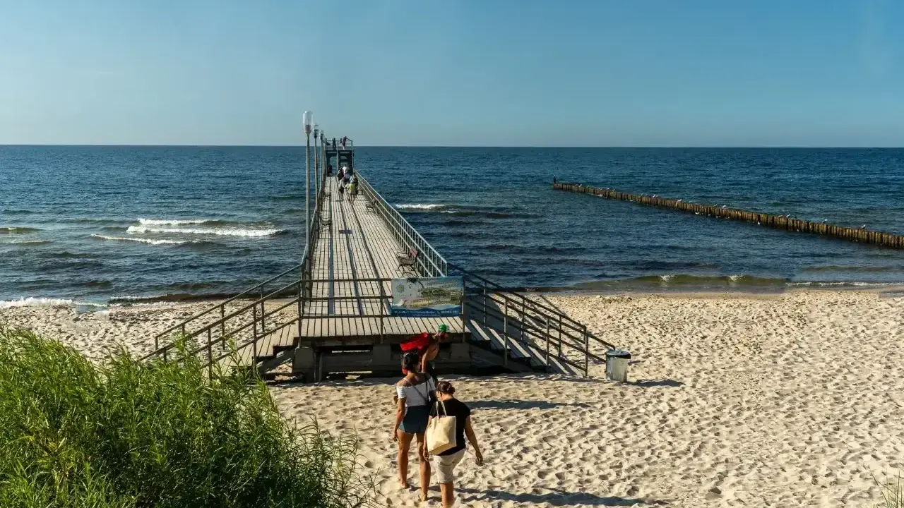 Sianożęty atrakcje: drewniane molo wchodzi w morze, plaża i fale.