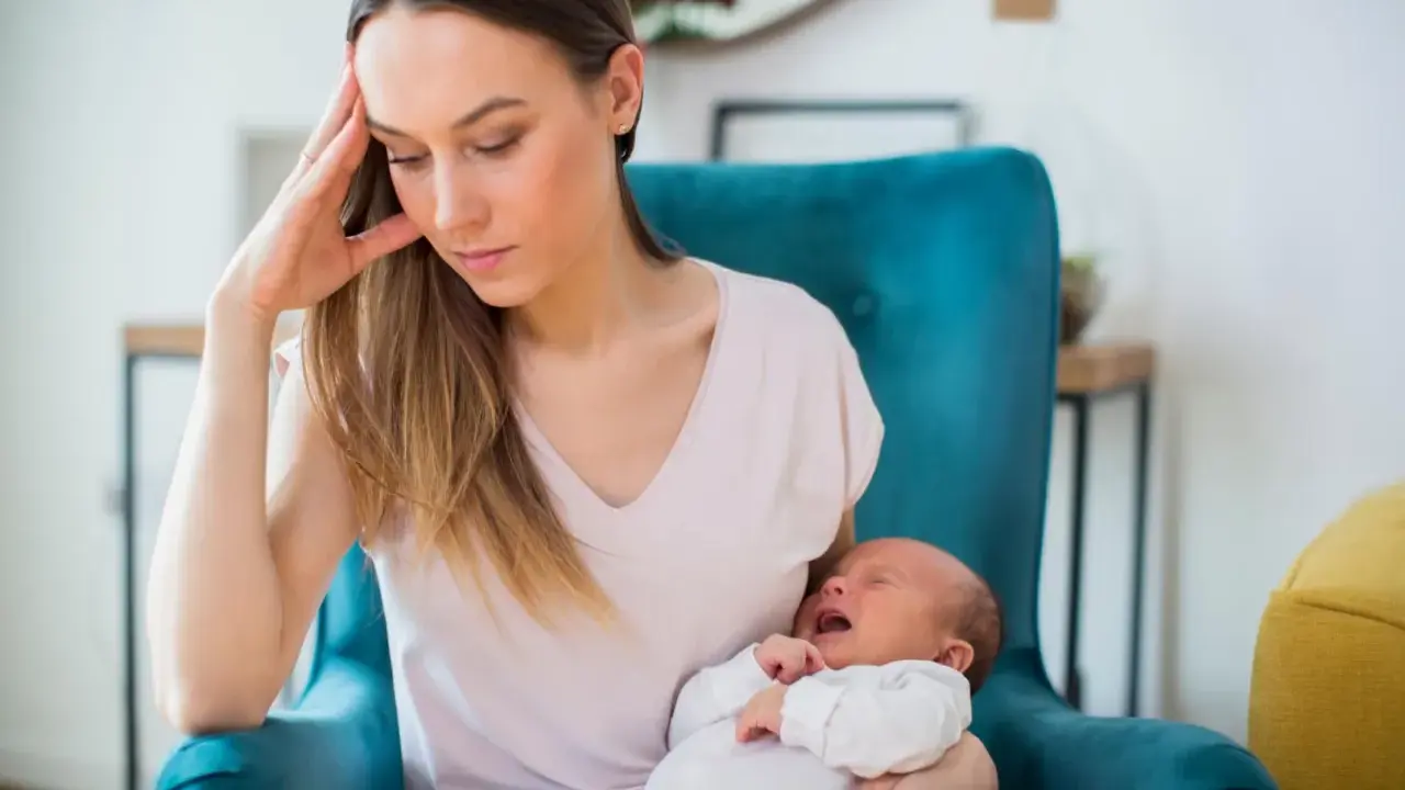 Zmęczona mama z płaczącym niemowlakiem na rękach, w fotelu, w poszukiwaniu siebie.