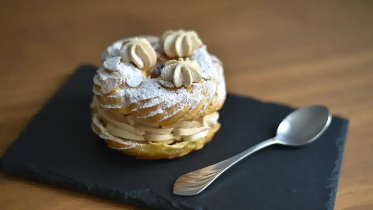 Un délicieux Paris-Brest saupoudré de sucre glace, prêt à être dégusté avec une cuillère.
