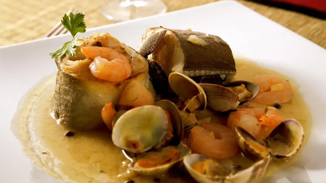 Delicioso abadejo a la donostiarra con gambas y almejas en una salsa dorada, adornado con perejil fresco.