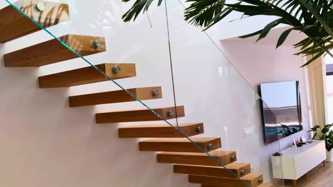 Escalera flotante de madera con **rejas de cristal** que aportan ligereza y modernidad al espacio.