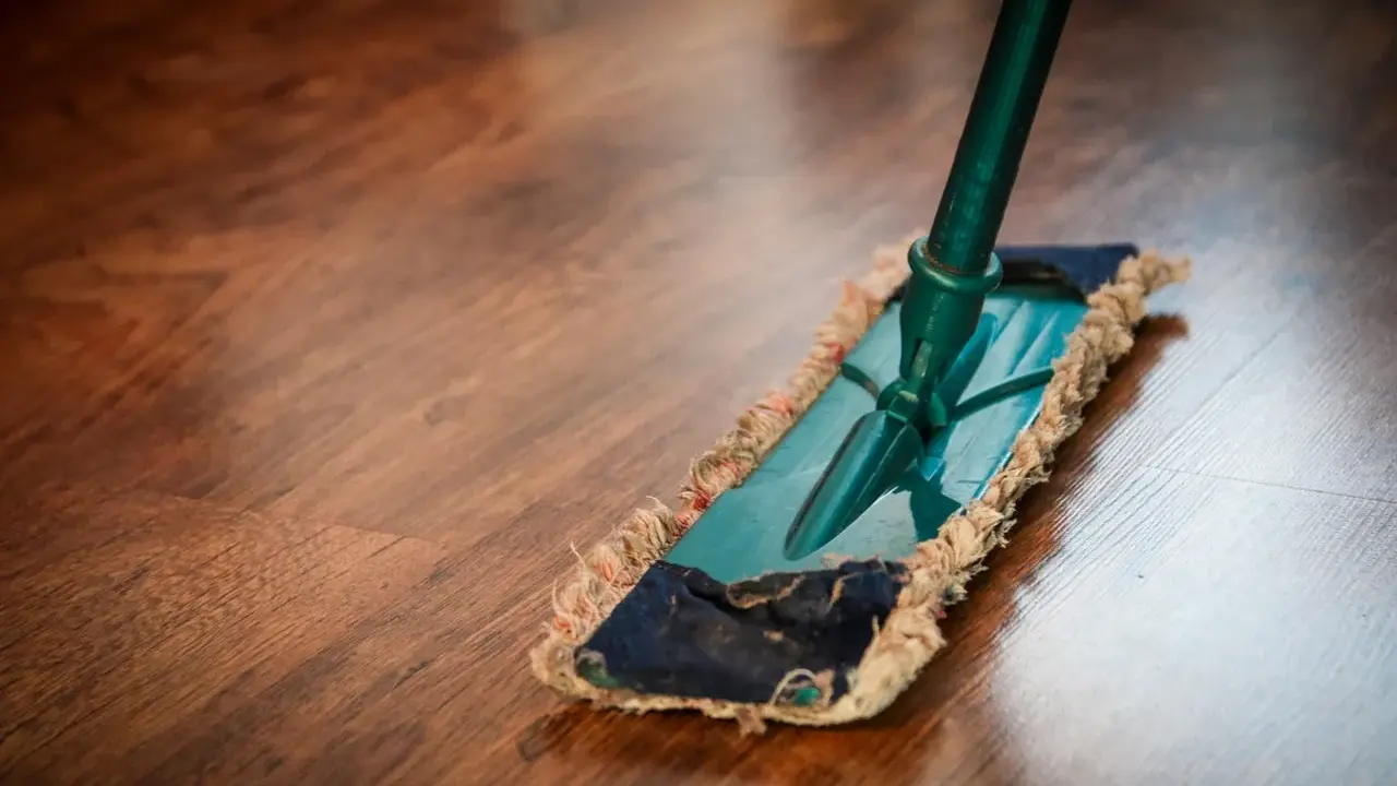 Ein Mopp reinigt einen Holzboden. Die richtige Parkett Pflege sorgt für Glanz und Langlebigkeit.