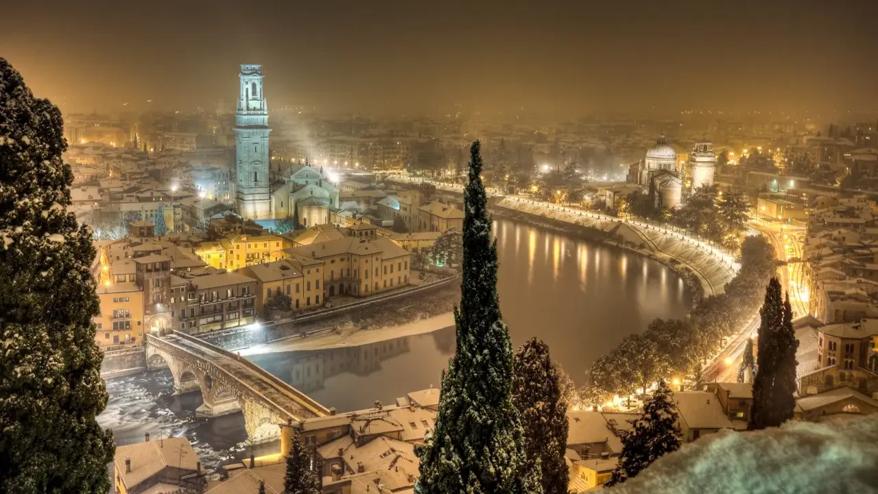 Verona innevata, un'incantevole **città da visitare a dicembre**. La neve copre i tetti e il fiume Adige riflette le luci della città.