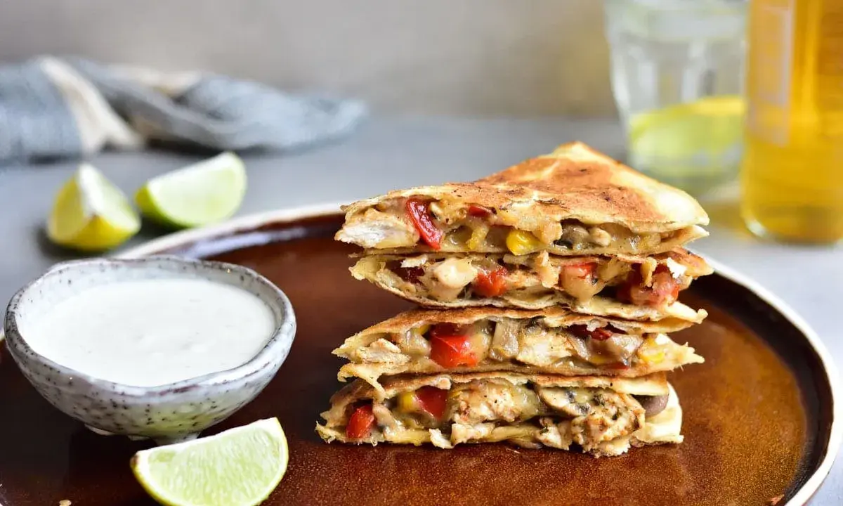 Stos **quesadilli z kurczakiem**, papryką i serem, podane z dipem i limonką.