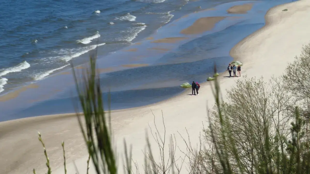 Plaża z falami, piaskiem i kilkoma spacerującymi osobami, widok z klifu.