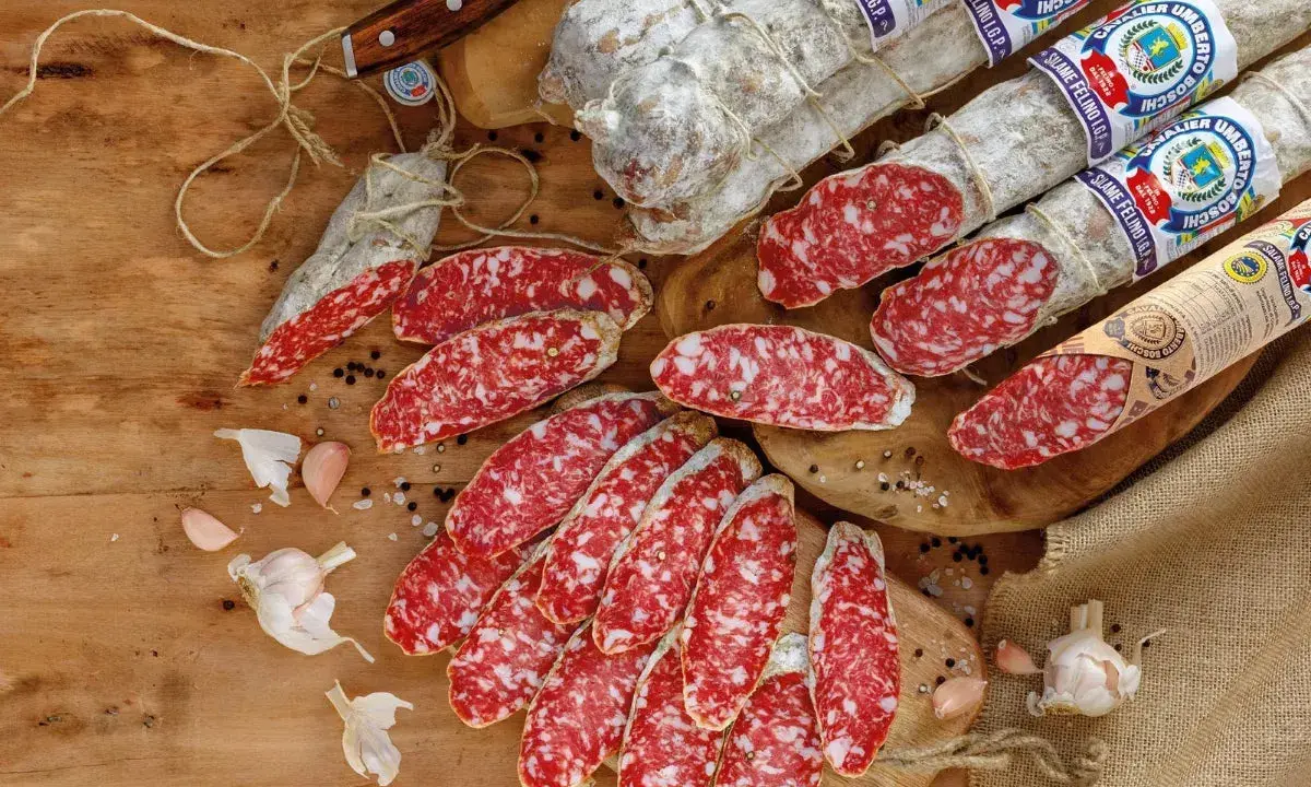 Eine Auswahl an italienischen Salami-Sorten, aufgeschnitten und im Ganzen, mit Knoblauch und Pfefferkörnern auf Holz.