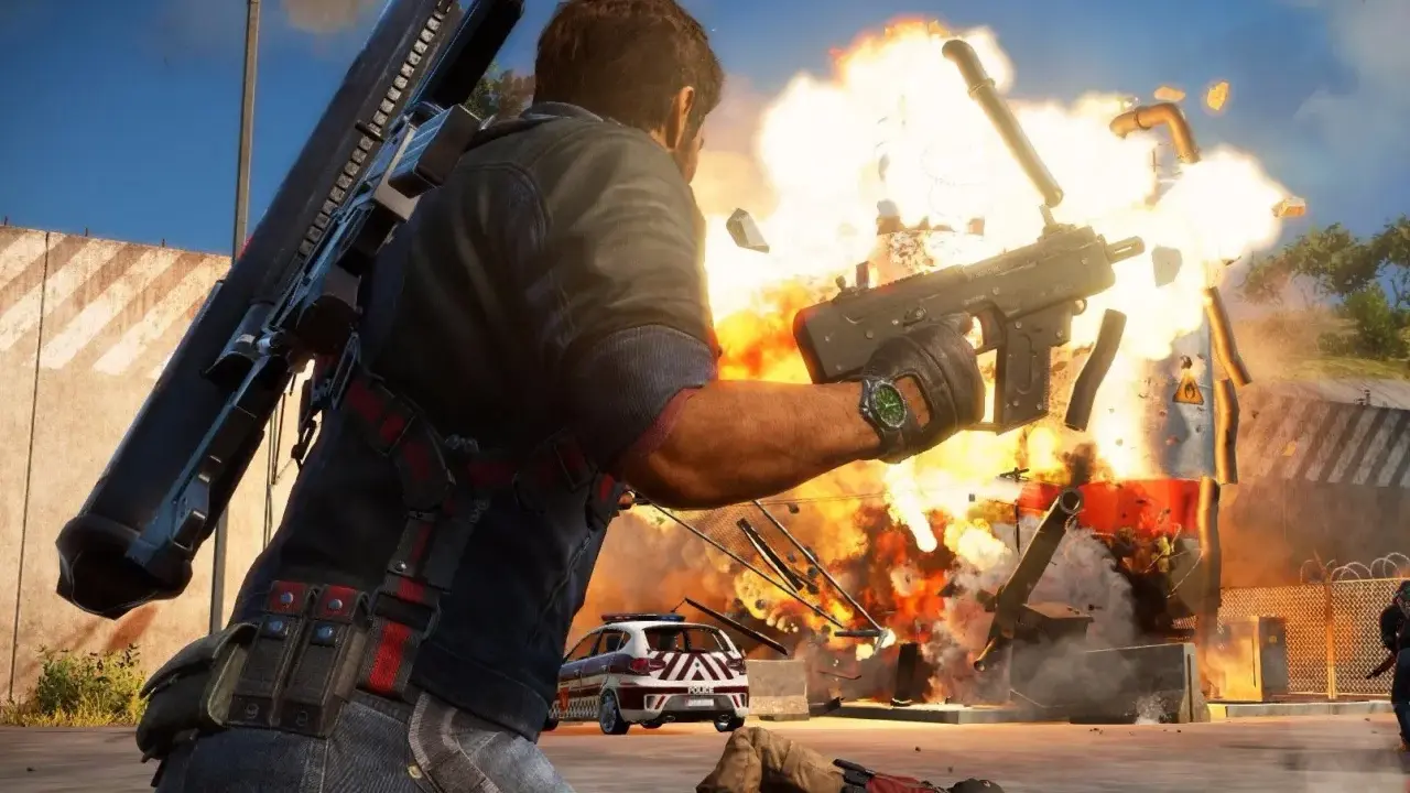 Rico Rodriguez strzela z pistoletu maszynowego, wywołując eksplozję. W tle radiowóz i powalony przeciwnik. Just Cause 3 wymagania.