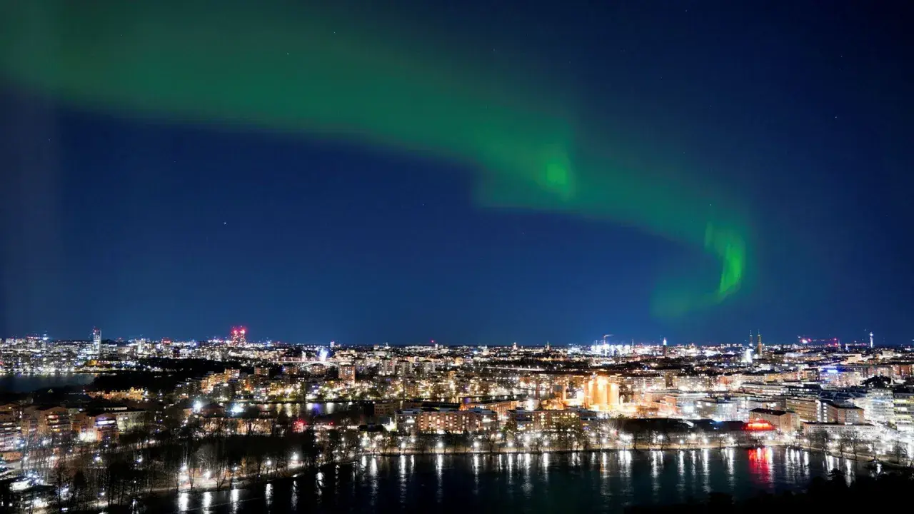 Grön norrsken dansar över ett upplyst Stockholm vid vatten.