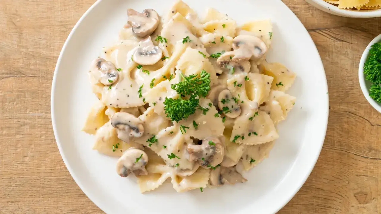 Szybki obiad z makaronem farfalle w kremowym sosie grzybowym, posypany natką pietruszki. Idealny na szybki posiłek.