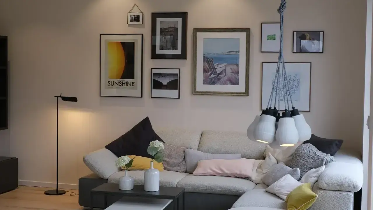 Przytulne mieszkania w Danii: salon z wygodną kanapą, galerią ścienną i designerską lampą.