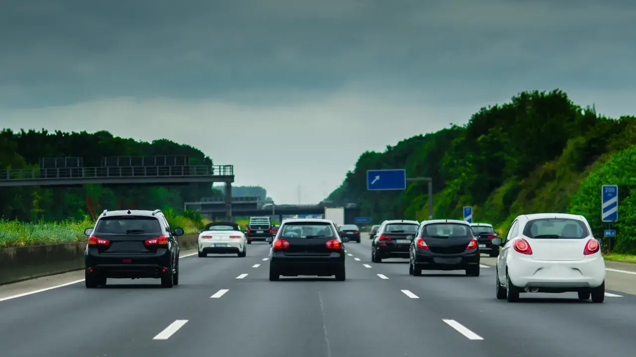 Ruch samochodów na niemieckiej autostradzie A8 pod pochmurnym niebem. Widać kilka czarnych i jeden biały samochód jadący pasem.