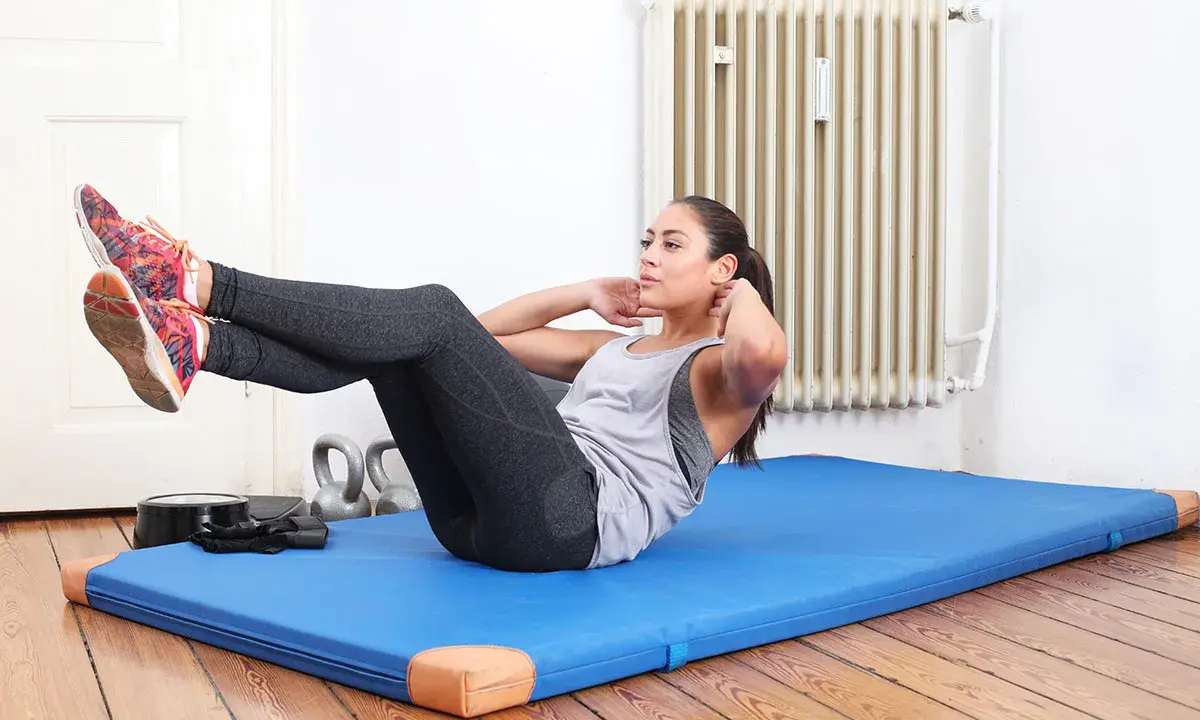 Frau macht Crunches auf einer blauen Matte. Sie trainiert ihren Bauchmuskel, um fit zu bleiben.