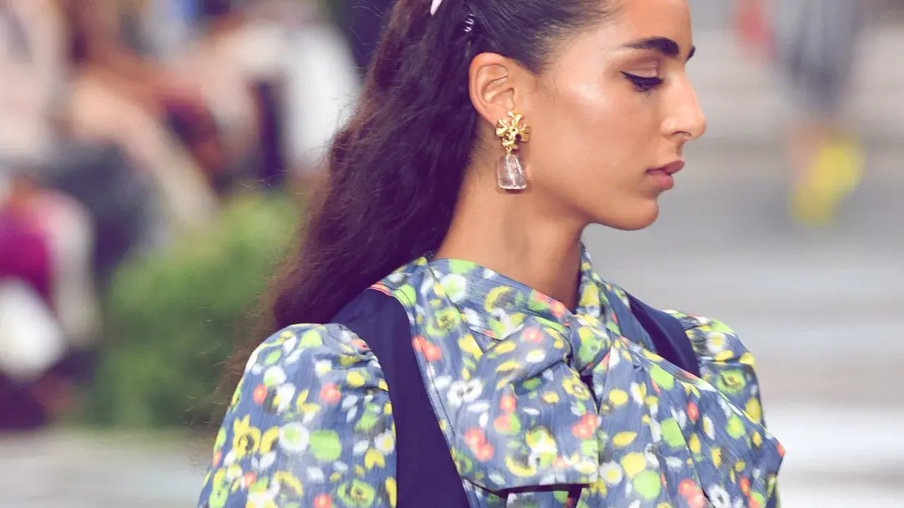 Ein dezenter Haarkamm hält die elegante Frisur einer Frau mit auffälligem Ohrring und geblümtem Kleid im Zaum.