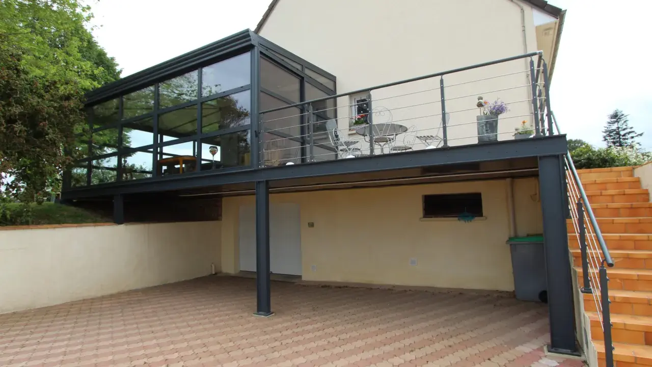 Modèle de véranda sur balcon avec structure métallique et vitrage. Un espace extérieur aménagé avec table et chaises.