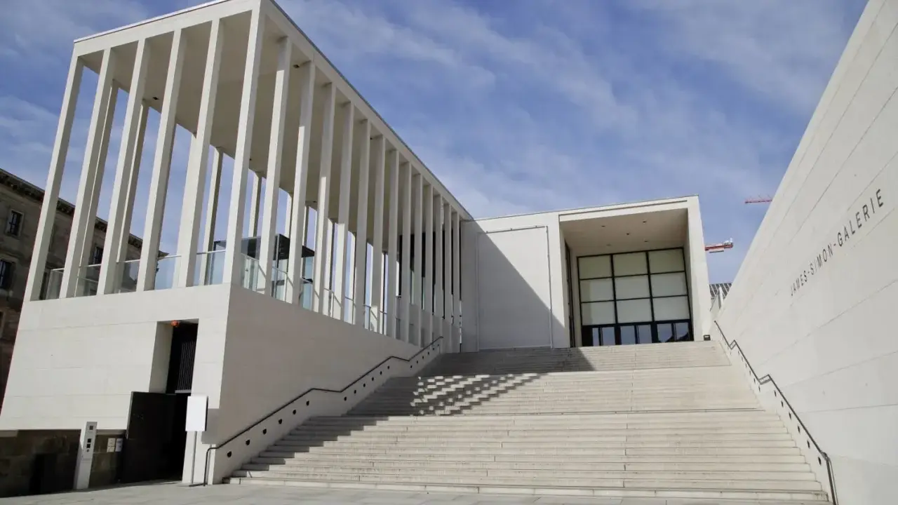 Moderne James-Simon-Galerie mit langer Treppe, ein Werk bekannter Architekten, vor blauem Himmel.