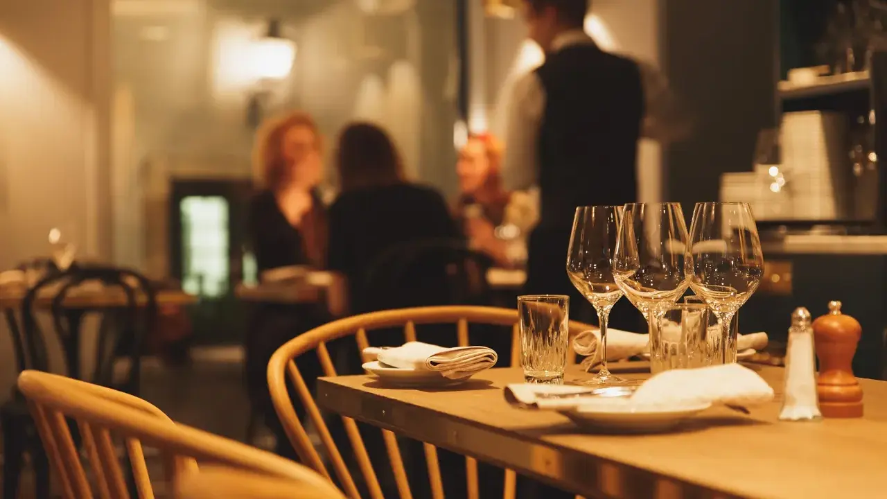 Ett dukat bord med vinglas och servetter, redo för en matvandring i Stockholm. I bakgrunden syns gäster och personal i en mysig restaurangmiljö.