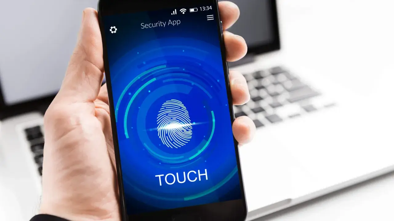 Dłoń trzyma smartfon z ekranem blokady "Security App" i ikoną odcisku palca. Proces autoryzacji jest w toku.