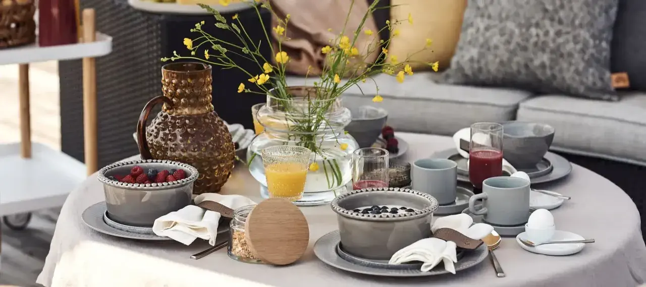 Vacker dukning runt bordet med frukostskålar, bär, juice och en vas med gula blommor.